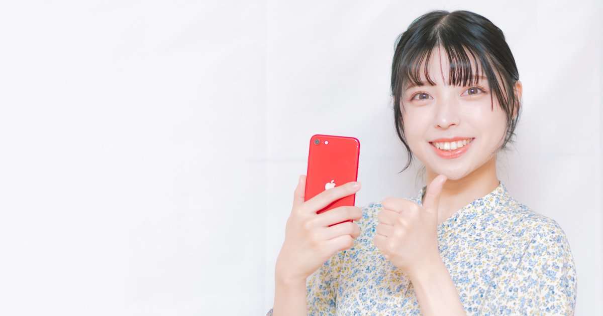赤いスマホを手に親指を立てて笑顔の女性