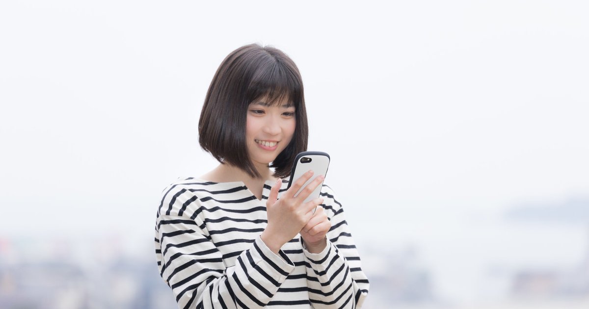 屋外でスマホを操作しながら笑顔の女性
