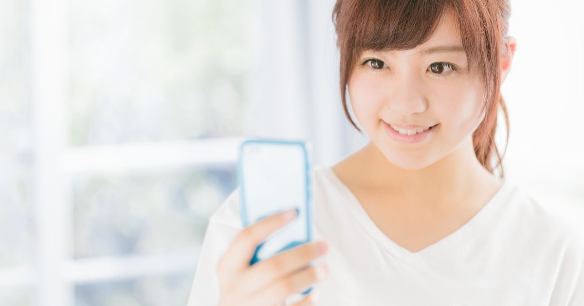 スマホの画面を見ながら微笑む白い服の女性
