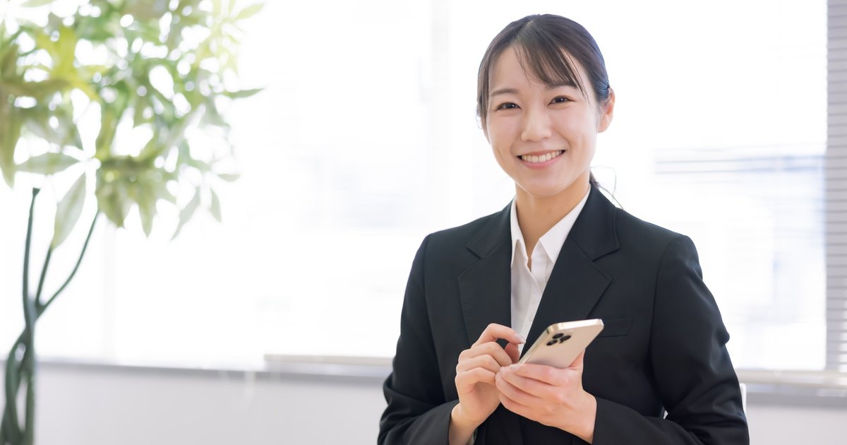 スマホを操作しながら笑顔で応対するスーツ姿の女性